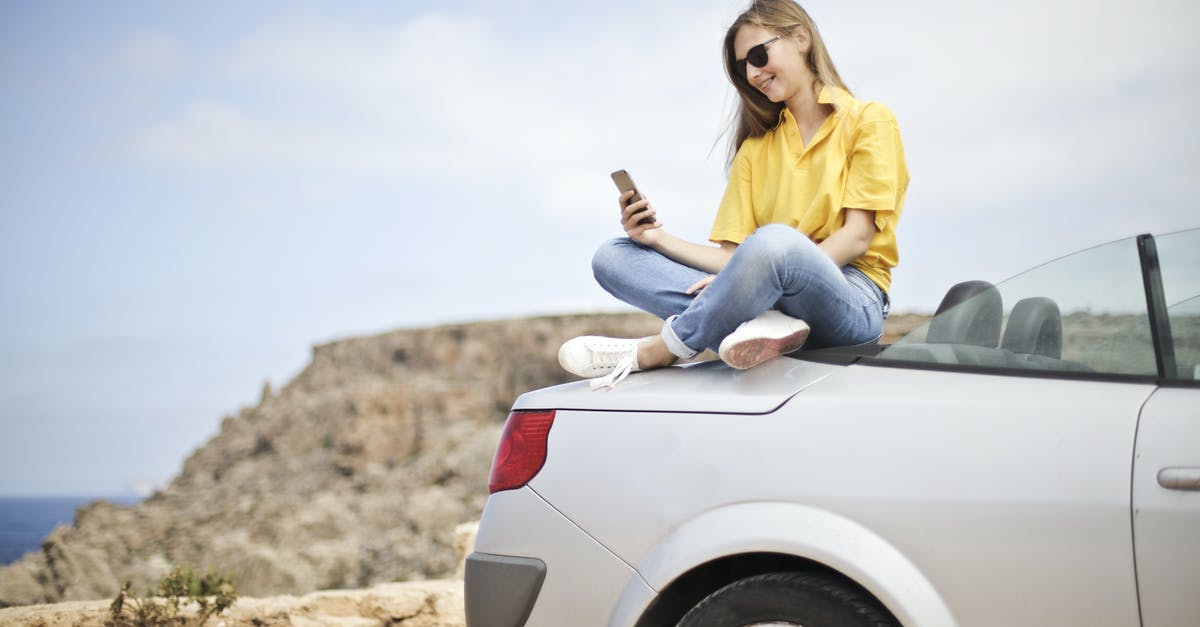 Traveling to Seoul, phone questions - Woman in Yellow Blouse and Blue Jeans Taking Selfie While Sitting on Car