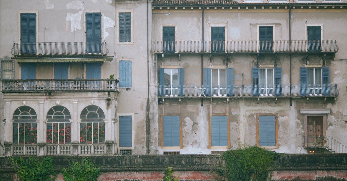 Traveling within Schengen area with a French resident card - Shabby old building decorated and windows with balconies and fence with green plants in city in daytime