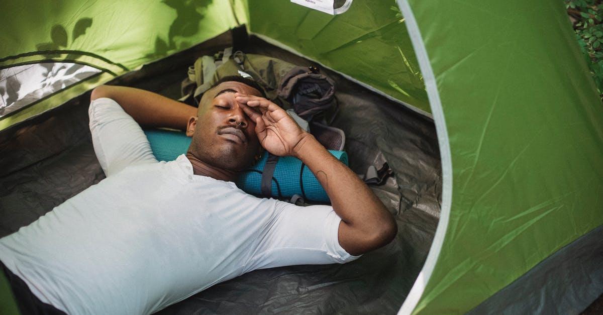Travelling from London to Paris and return journey [closed] - From above of calm African American male traveler with closed eyes resting in tent and rubbing eyes during nap