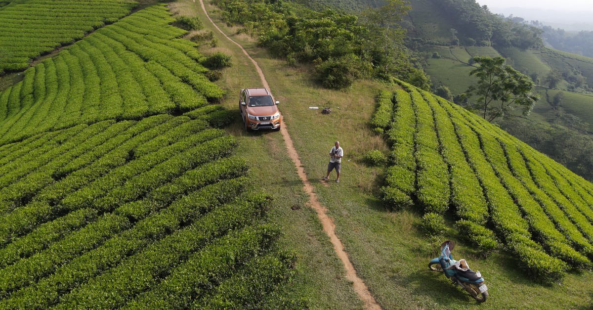 Travelling From London to Vietnam being Spanish, Visa issues? - Drone view of SUV car and motorcycle parked near unrecognizable male traveler standing on green hill with tea plantations during trip in Vietnam