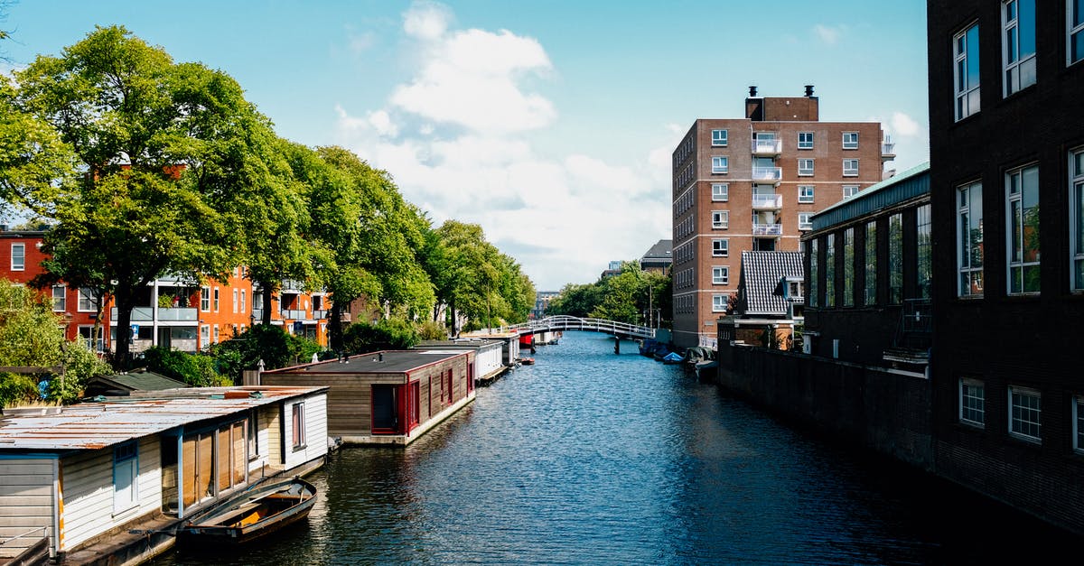 Travelling Netherlands and Belgium on a budget -- need trip feedback [closed] - Picturesque channel in Amsterdam with traditional houseboats near modern buildings in city outskirts against blue sky