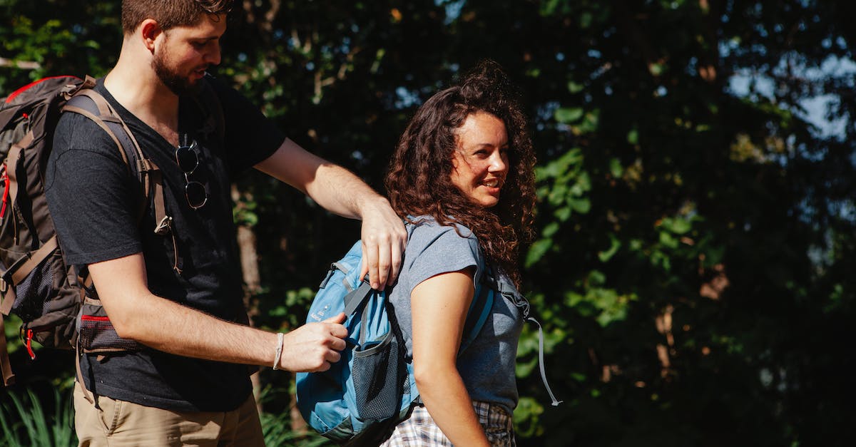 Travelling to Israel - help to divide time between areas [closed] - Side view of young bearded male hiker closing rucksack of cheerful female beloved against green trees