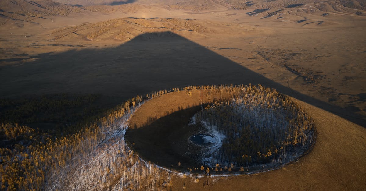 Travelling to Kyzyl, Tuva from Mörön, Mongolia - Aerial view of Khorgo extinct volcano grown with forest and covered with snow casting huge dark shadow on valley in national park in Mongolia