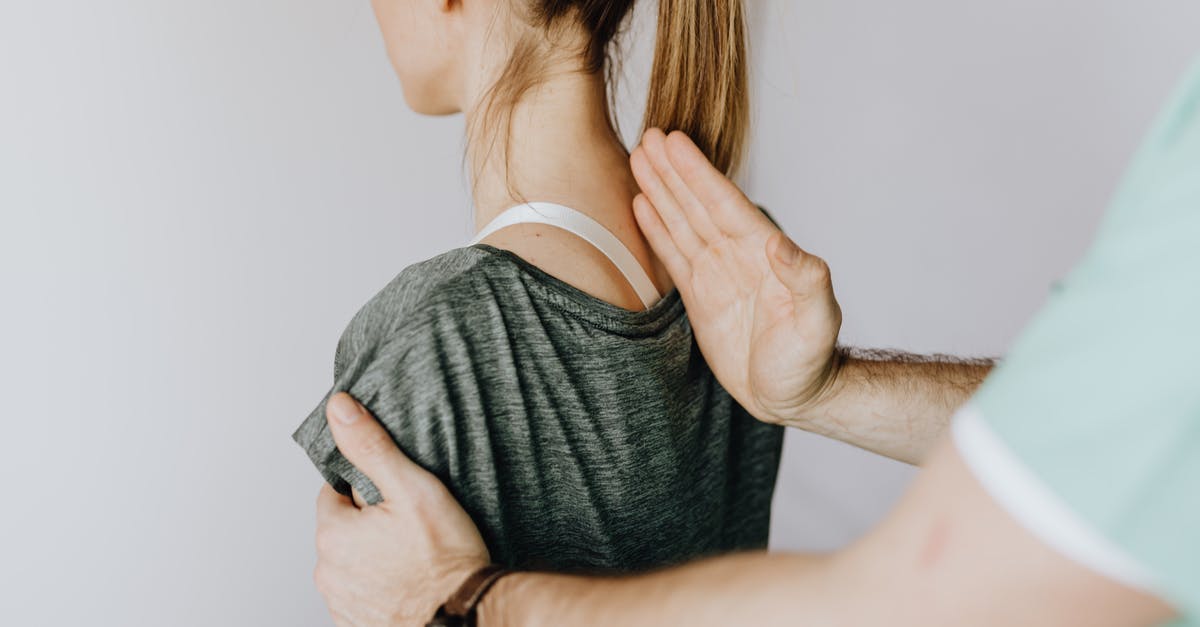 Travelling to UK and back to visit sister in transit-area - Back view of crop unrecognizable osteopath in uniform and wristwatch checking up back of slim female patient in casual wear on white background