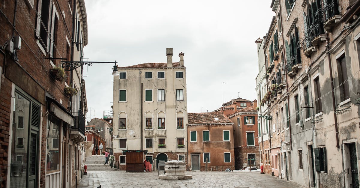 Travelling to Venice on All Saint's day - Old paved street with shabby stone buildings decorated with windows and small balconies of different sizes and shapes on overcast day