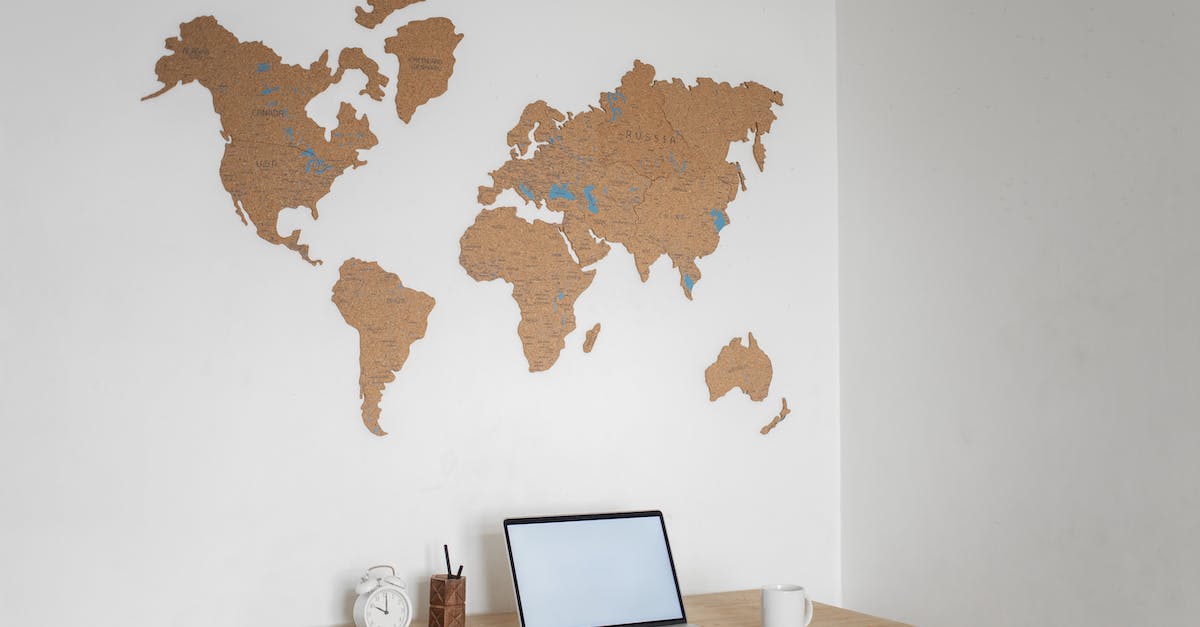 Travelling with a laptop - Wooden table with modern netbook with blank screen and alarm clock placed at white wall with decorative world continents in light room