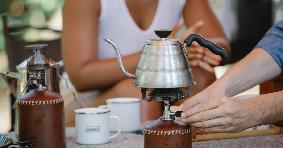 Travelling with a portable Stove and fuel canisters - Crop couple heating metal kettle on camp stove