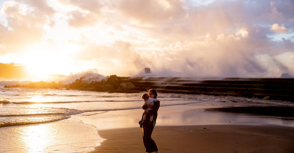 Travelling with beach sand in carry-on - Woman Standing on Seashore Carrying Her Child during Sunset