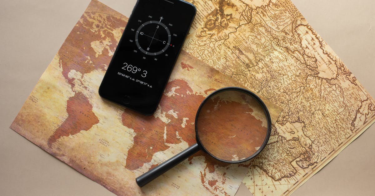 Travelling with research equipment - Top view of magnifying glass and cellphone with compass with coordinates placed on paper maps on beige background in light room