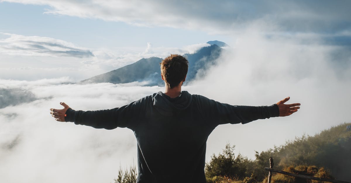 Trekking in Georgian Tusheti region? Safety? - Back view of anonymous male traveler in casual clothes standing on edge of cliff and admiring breathtaking scenery of clouds and mountain top