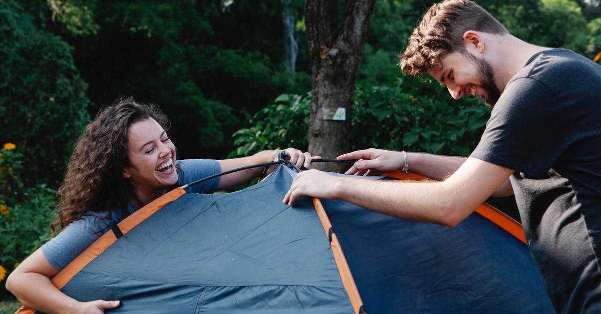 Trekking in Nepal [closed] - Cheerful young couple in casual clothes laughing while setting up camping tent during romantic picnic in nature