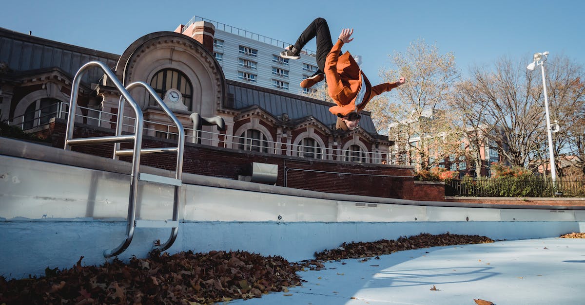 Trick to breaking down air routes - Side view of agile male athlete performing break dance backflip while jumping in air under blue sky in autumn town