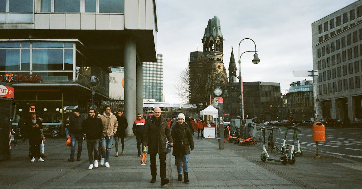 Trip in the south of Germany [closed] - Full body of anonymous people in warm clothes walking on paved pedestrian street near modern buildings and ancient Kaiser Wilhelm Memorial Church in Berlin