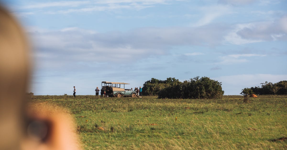 Trip to iceland: paying for tours or taking bus/car - Unrecognizable person shooting picturesque landscape of grassy savanna and tourists standing near parked safari automobile on summer sunny day