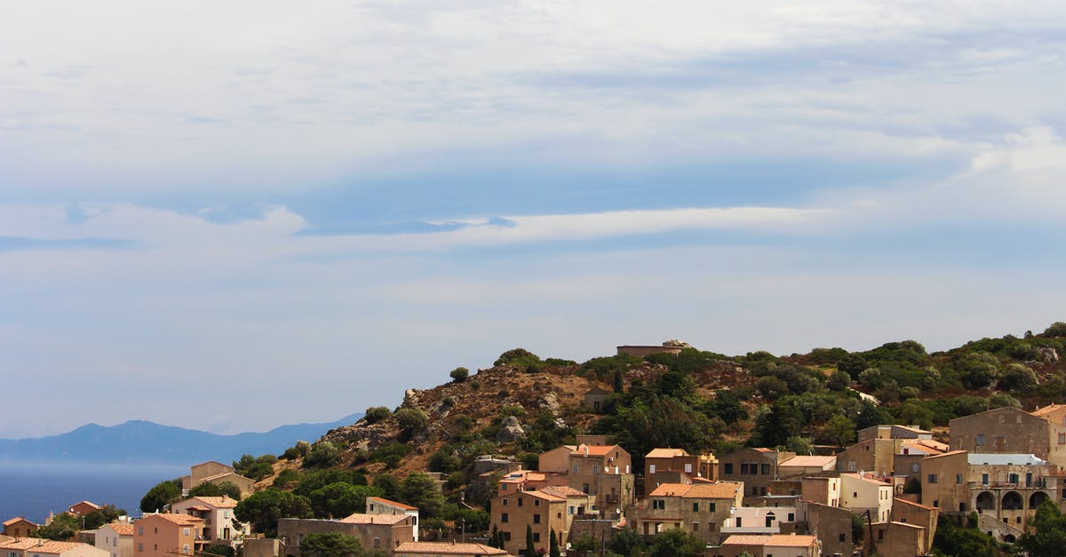 Trip to India from Abu Dhabi for an UAE residence - From above of small aged residential houses located on hill among green vegetation against cloudy sky in highland in nature