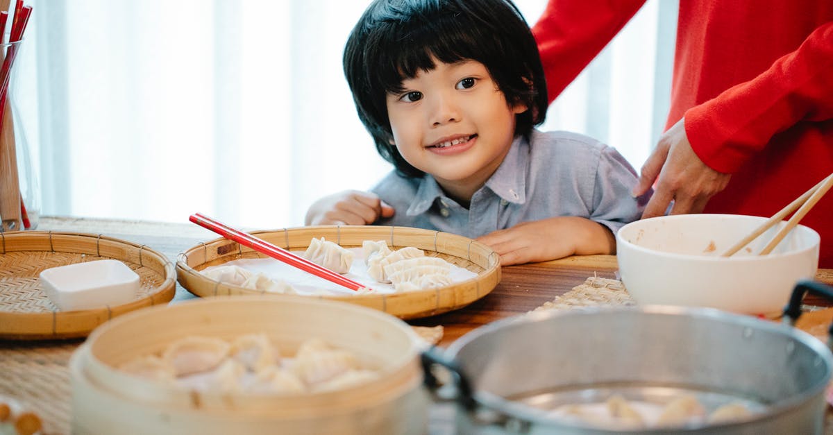 Trying local Romanian cuisine in Bucharest [closed] - Positive ethnic boy sitting at table with homemade Chinese dumplings on bamboo plates for steamer