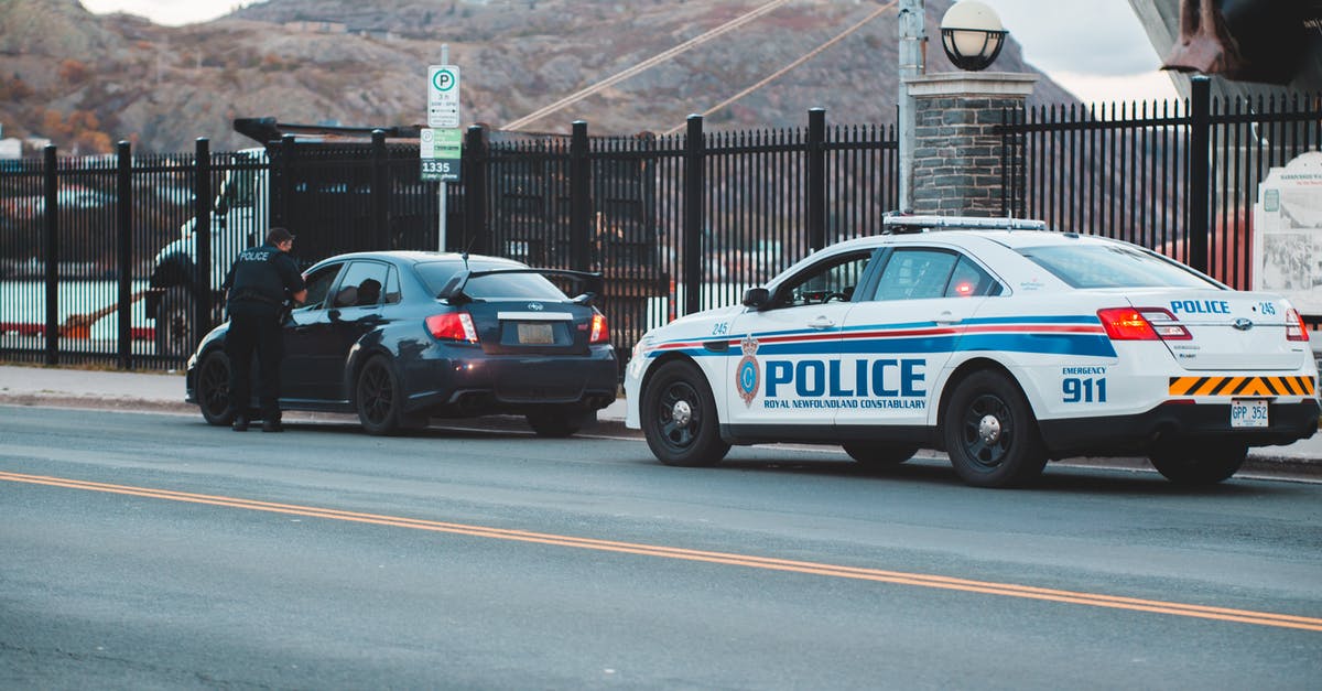 TSA Security Check - Flammable vs. Non-Flammable Aerosol - Back view of unrecognizable police officer in uniform checking modern car parked on asphalt road against cloudy sky