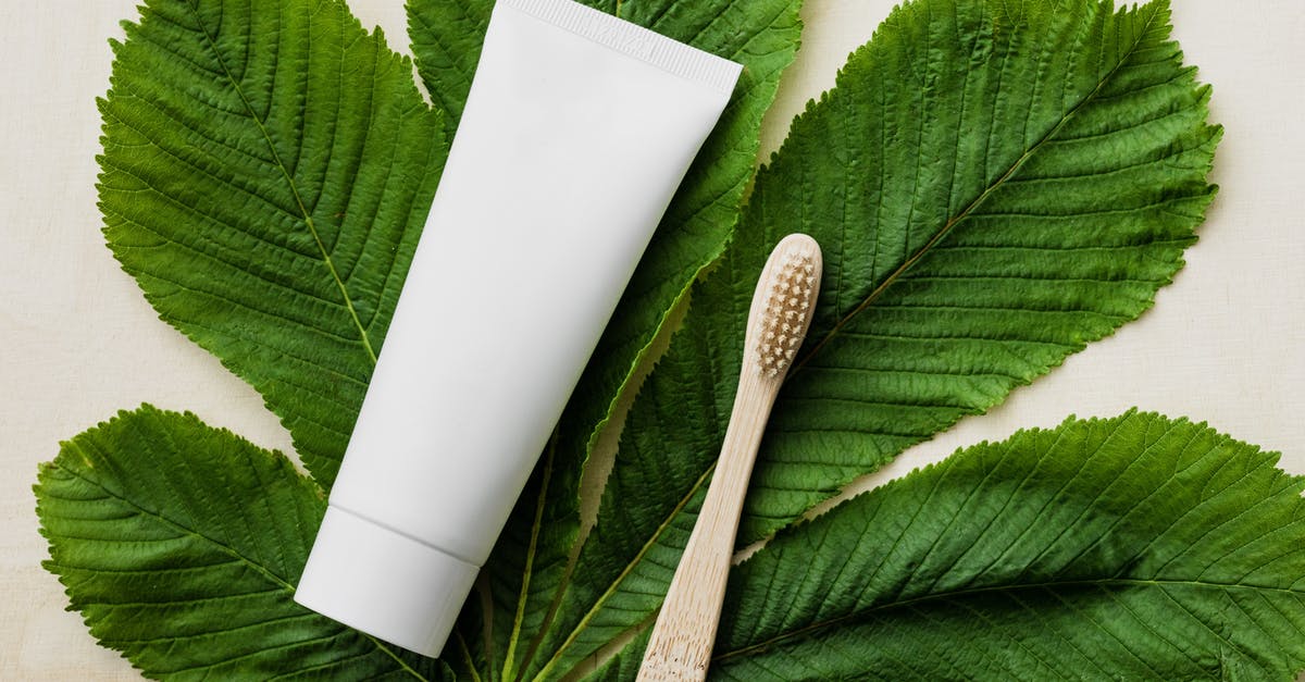 Tube from Heathrow to King's Cross - Top view of white mockup tube of natural toothpaste and eco friendly bamboo toothbrush placed flat on big green chestnut leaf on light wooden surface