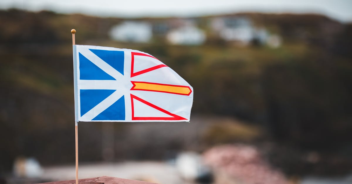 Two international connections from India to Canada via Bangkok and Tokyo - Waving national flag of Newfoundland and Labrador placed on wooden fence against blurred coastal settlement on hilly terrain