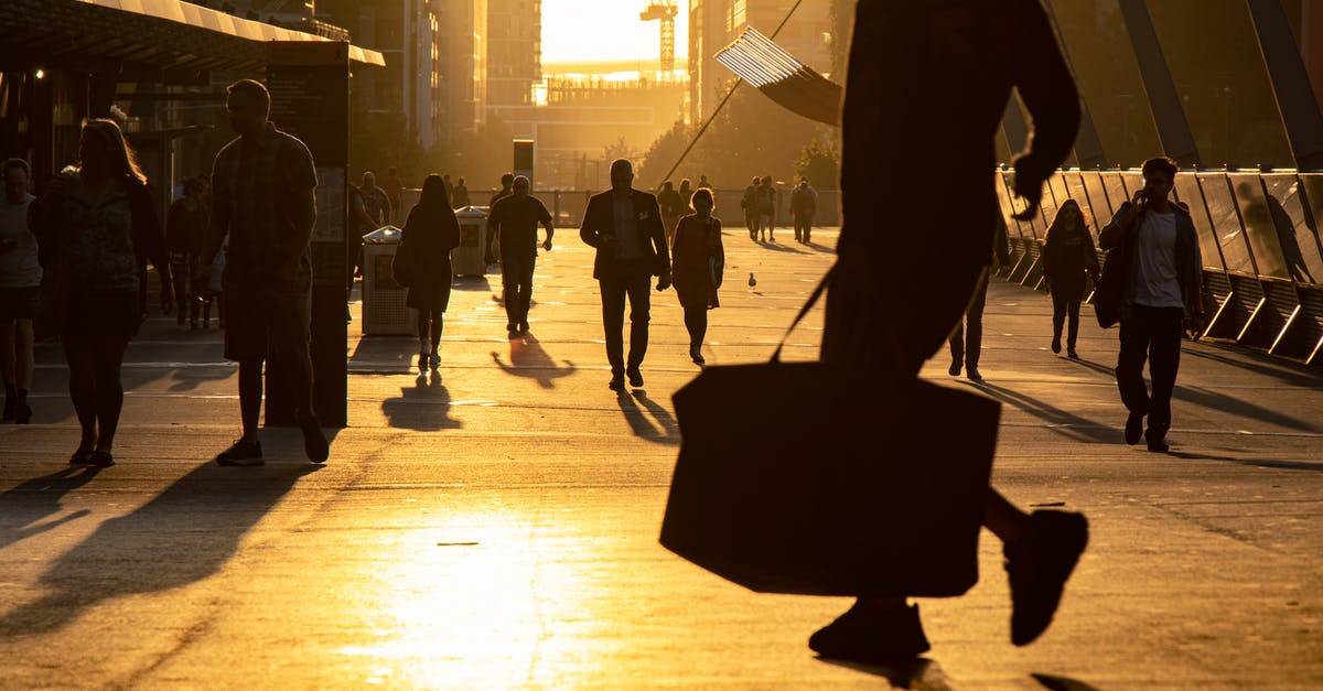 Two people travelling from different departures to the same destination? - People on crowded wide busy street in downtown walking along in city in evening