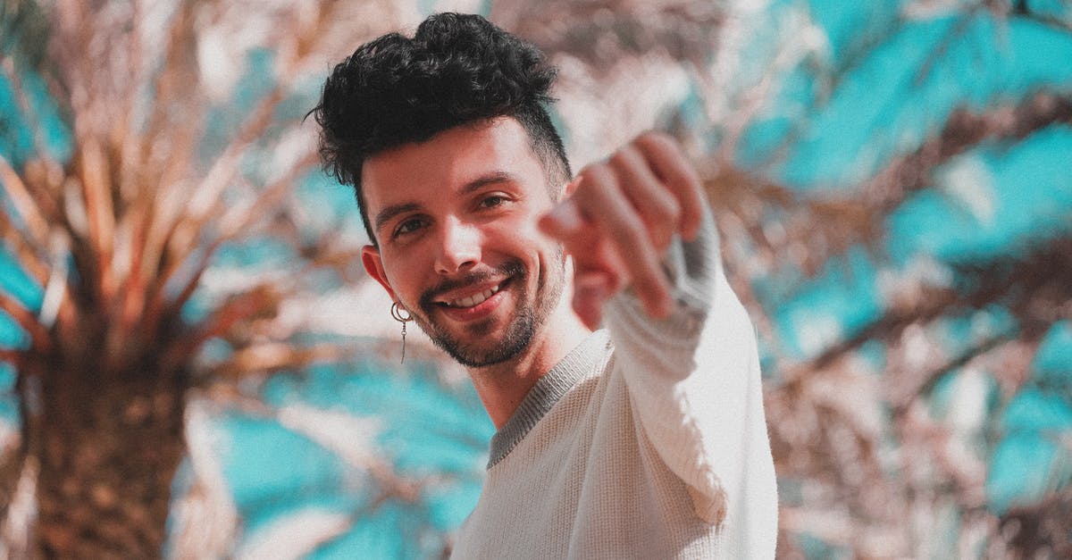 Uber -- do you get rewards points when adding funds? - Low angle of modern trendy man with earring pointing with finger at camera standing under palm trees in sunshine