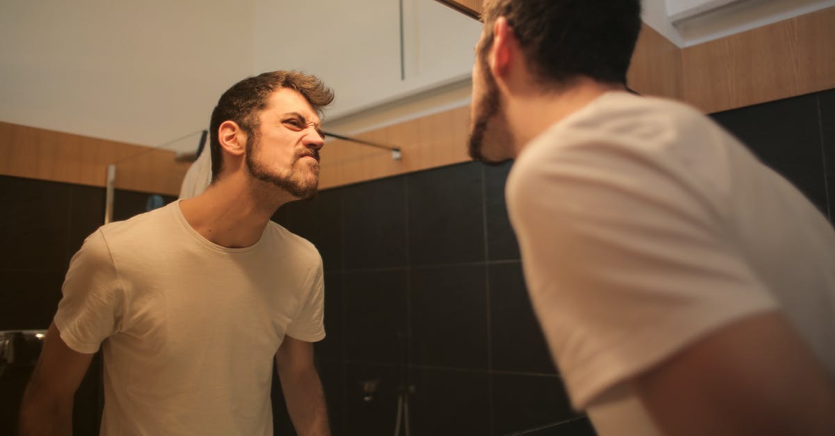 UK extended family visa question - Low angle side view of young bearded male in casual shirt standing in bathroom and looking at with frown mirror in morning