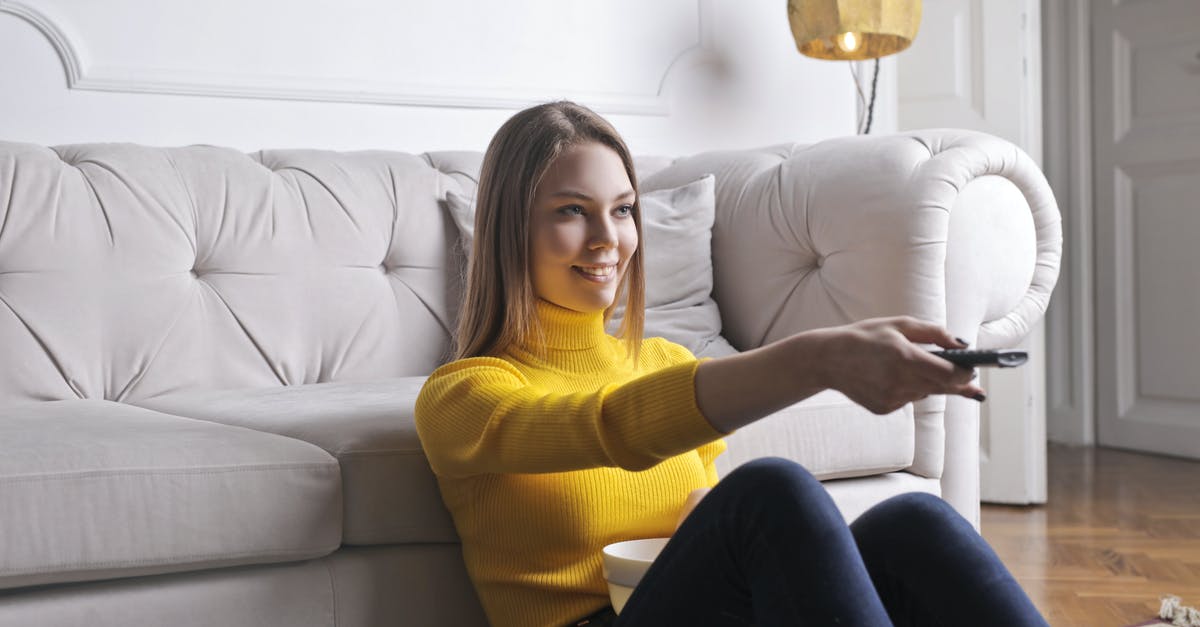 UK extended family visa question - Joyful millennial female in casual clothes with bowl of snack using remote controller while sitting on floor leaning on sofa and watching movie in cozy light living room with luxury interior