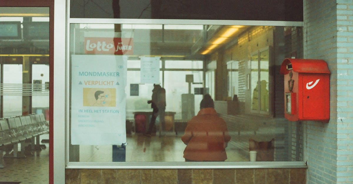 (UK rail travel) Where can you exchange a Permit to Travel for a ticket? - Through glass of anonymous tourists in warm outerwear standing in waiting room of modern railway station (UK rail travel) Where can you exchange a Permit to Travel for a ticket? - Through glass of anonymous tourists in warm outerwear standing in waiting room of modern railway station
