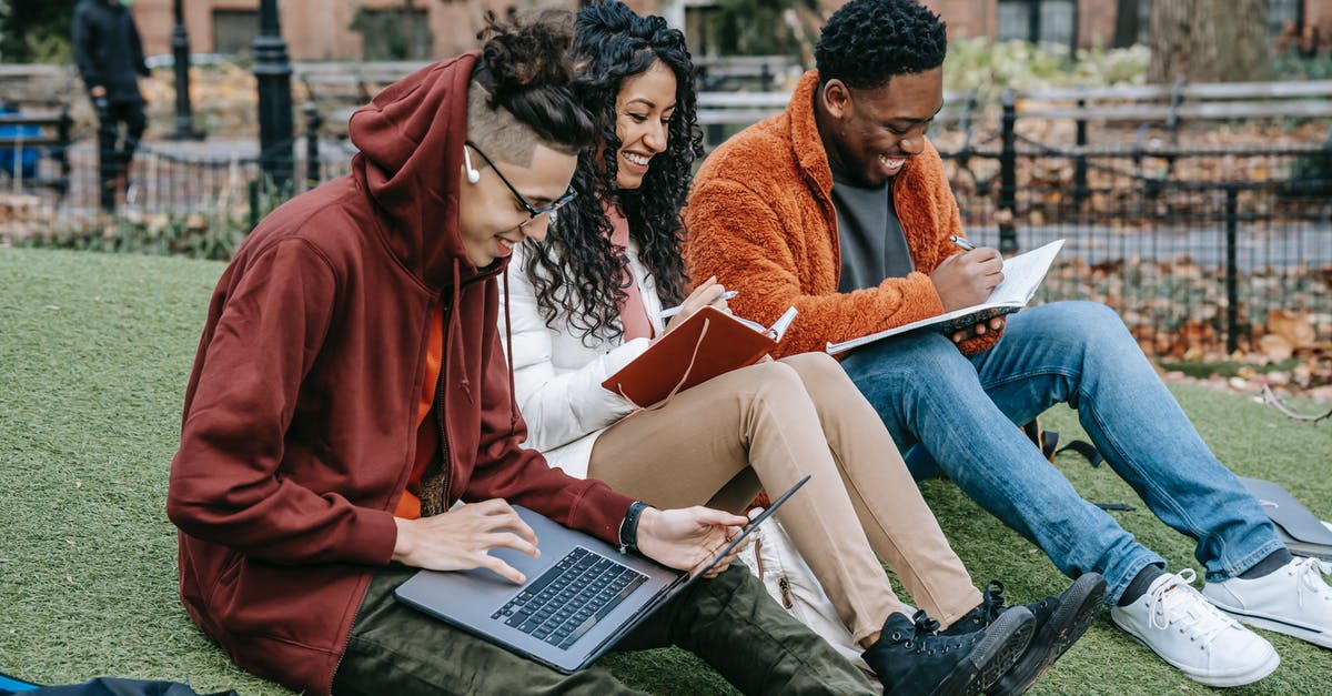 UK short-term study visa - group - Happy multiracial group of students in casual clothes sitting together on grass and studying with laptop and books