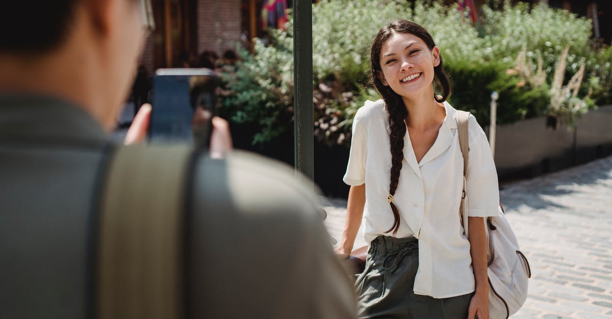 Uk Tier 5 Youth Mobility Visa arrival dates - Anonymous guy photographing happy Asian girlfriend on smartphone on city street