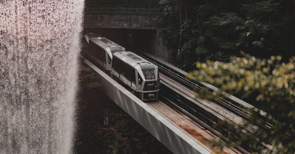 UK transit visa under processing; change of travel dates? - Scenic view of modern fast train going along railroad under waterfall bridge near lush forest trees on sunny day