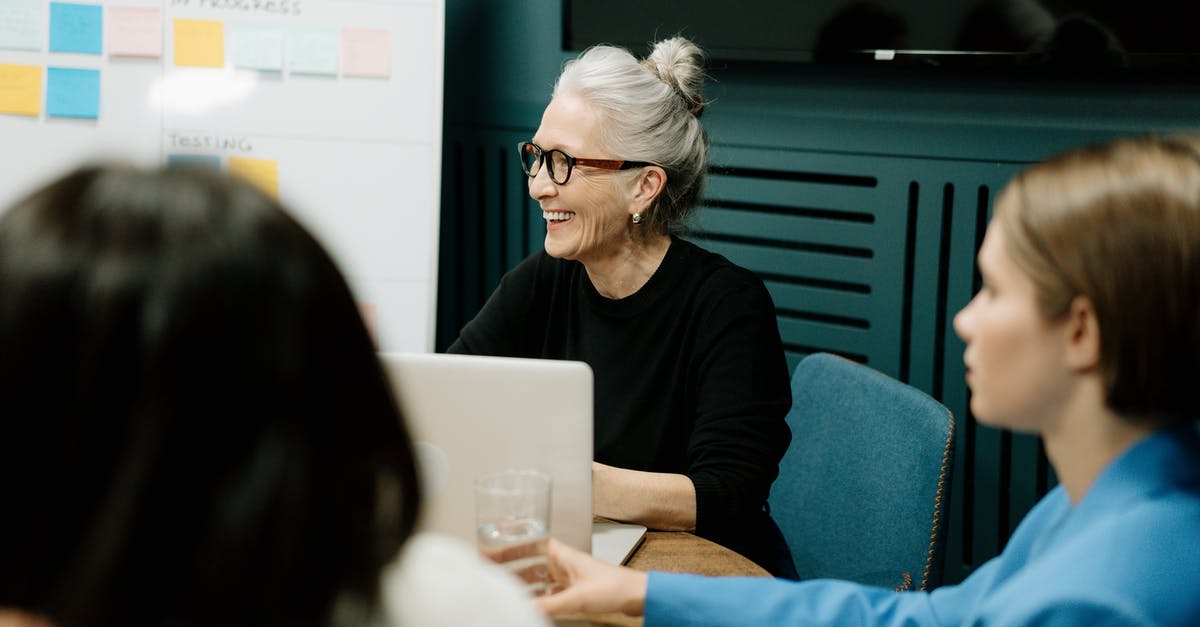 UK Visa application for conference - Self employed - Woman in Black Sweater and Eyeglasses Sitting on Chair Beside Woman in Blue Shirt