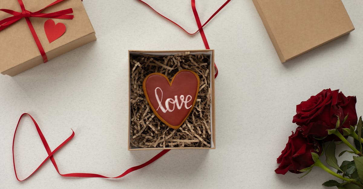 UK Visa form filling - Top view of heart shaped cookie with Love word in box with decorative paper filling [laced on gray background near gift boxes with red ribbons and bouquet of roses