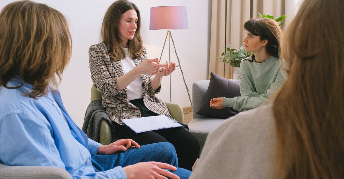 UK Visa group appointment - Young female therapist sitting on chair and discussing problem with patients during psychotherapy session in group