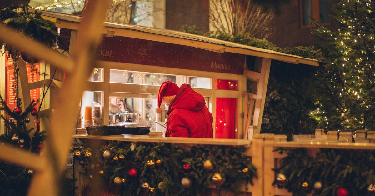 Unable to buy travel insurance for Kosovo in New Zealand - Back view of male wearing warm outerwear standing near counter at Christmas fair while enjoying holidays and purchasing takeaway beverage in illuminated city