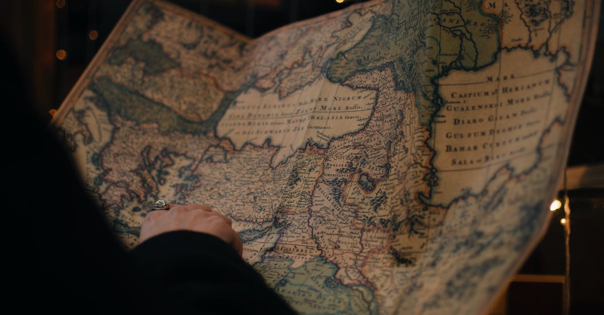 Unique travel destination research methods - From behind anonymous person examining antique world map printed on large paper in blue colors in dark room