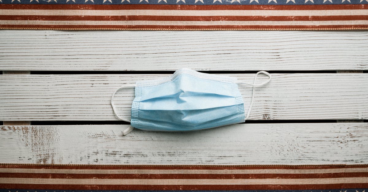 United Airlines online check-in for international departures from the US - Top view of sterile face mask placed on white shabby wooden table with American flag ribbons