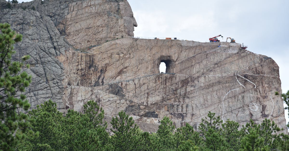 United States National Radio Quiet Zone: Impact on travellers? - Majestic steep Mount Rushmore surrounded by coniferous trees under light blue sky covered with clouds
