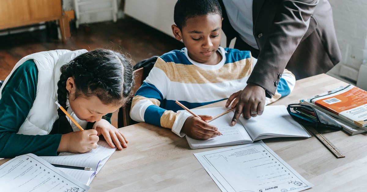 Unknown entry point for Schengen visa - High angle of crop unrecognizable black female teacher explaining task to focused little schoolboy sitting at desk near attentive Asian classmate writing in notebook