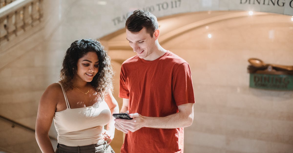 US Customs and connection time - Positive young multiethnic couple browsing smartphone during trip in New York