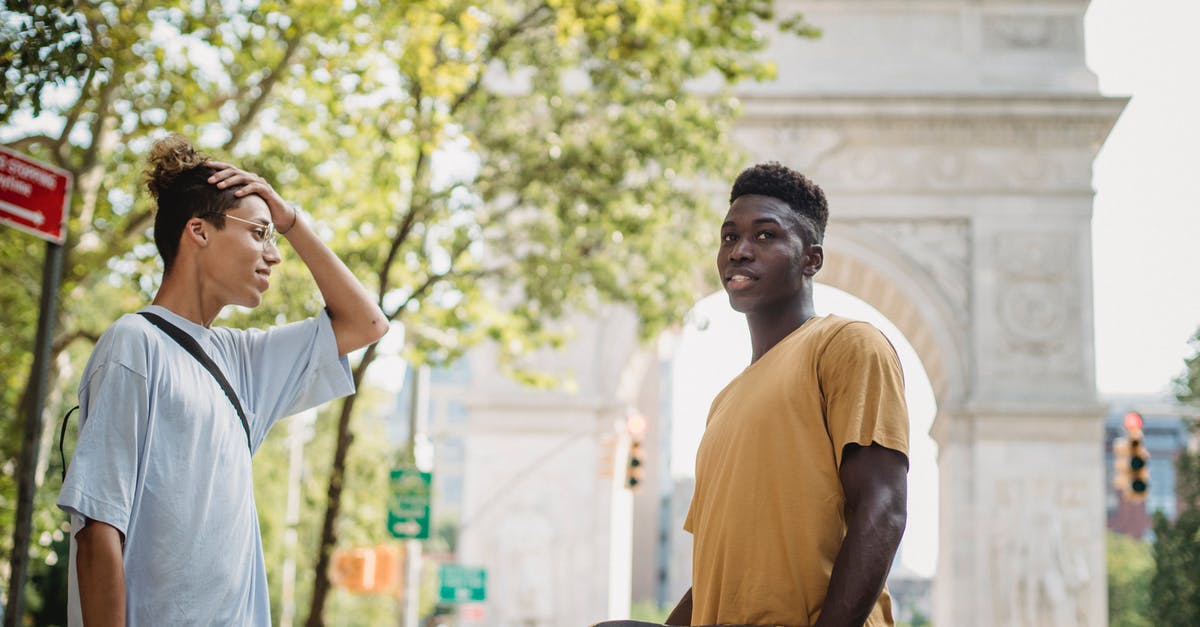 US Preclearance time at Abu Dhabi - (AUH - MAN - ORD) - Side view of young diverse male millennials in casual clothes standing on New York street near Washington Square Arch with skateboards in hands and chatting