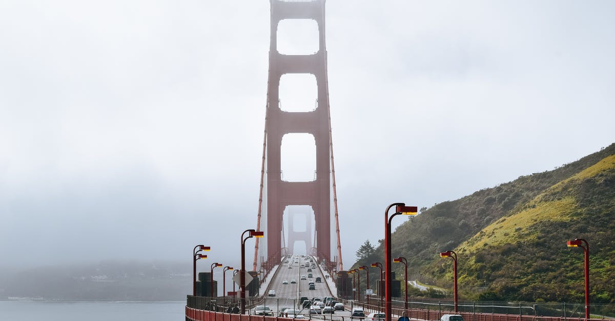 USA car rental one-way fee - Golden Gate Bridge with cars driving on roadway along green hills in dense fog