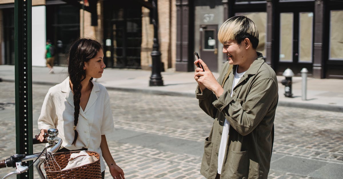 Use bike sharing service as a foreign tourist in China - Happy ethnic man taking photo of girlfriend standing on street near bicycle