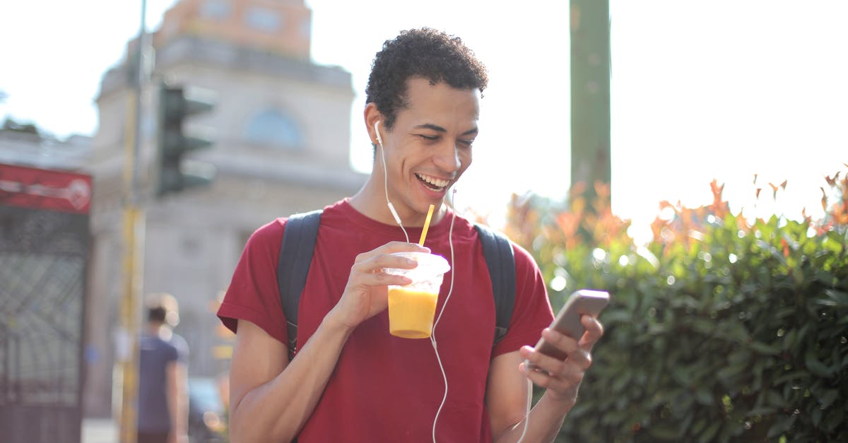 Use Travel Visa Before Using Student Visa? US to Europe - Happy ethnic guy in casual wear and with backpack having cup of fresh juice using smartphone while standing on street and listening to music