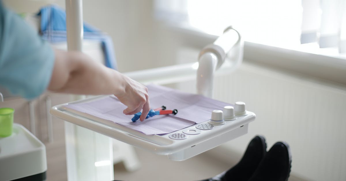 Using a C-Visit multiple visa to get medical treatment - Crop faceless dentist in blue uniform using dental tools and modern equipment while working with patients in dental clinic