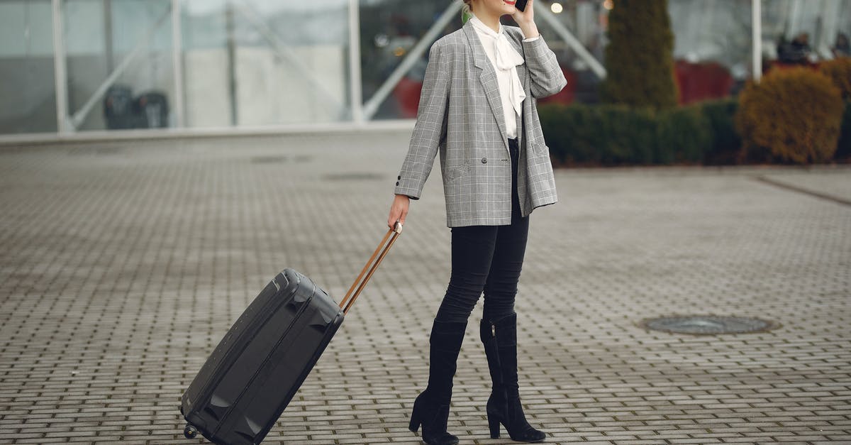 Using a multiple-entry business Schengen visa for tourism - Full body of elegant female tourist in stylish clothes standing with suitcase and calling taxi by phone after arrival in modern city