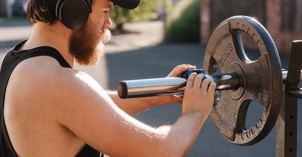 Using airline headphones with own equipment (during a flight) - Crop hipster sportsman preparing barbell before exercising on street