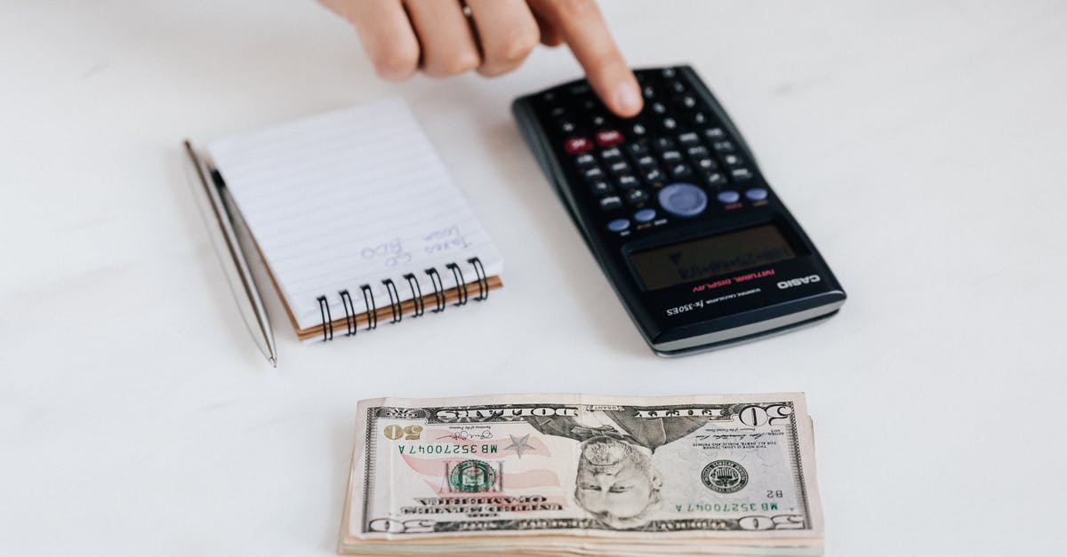 Using American Airline Miles - Top view of crop faceless economist touching calculator button while counting income near heap of paper bills and small notebook with pen