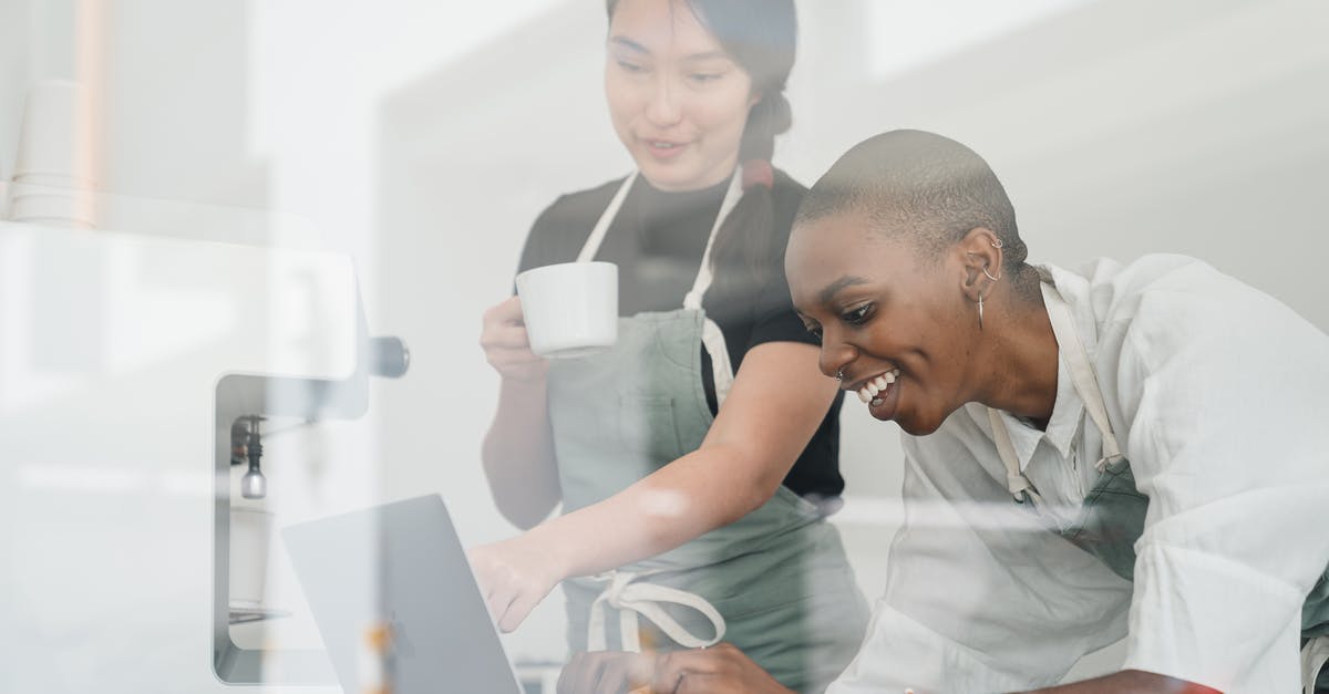 Using APC kiosk with new ESTA/passport - Through glass of friendly young Asian head barista showing young cheerful African American female coworker how to use special program on laptop