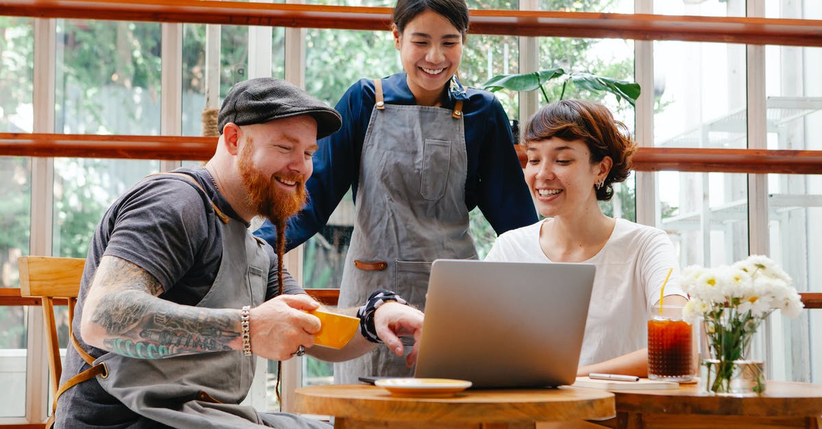 Using local transportation in Malta? - Positive coworkers in aprons and casual outfit using computer in cafeteria at table with coffee cup and glass of drink in day